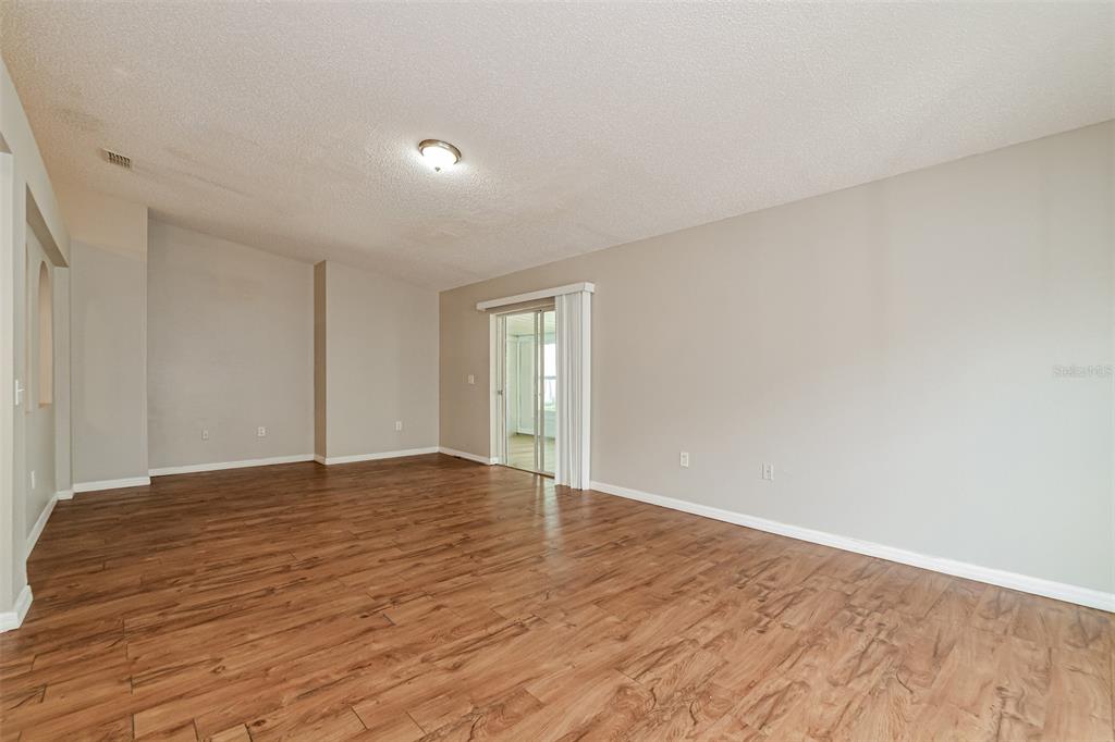 An empty living room features wood-look flooring, light gray walls, and a sliding glass door — 207 RONALDALE AVENUE, HAINES CITY, FL