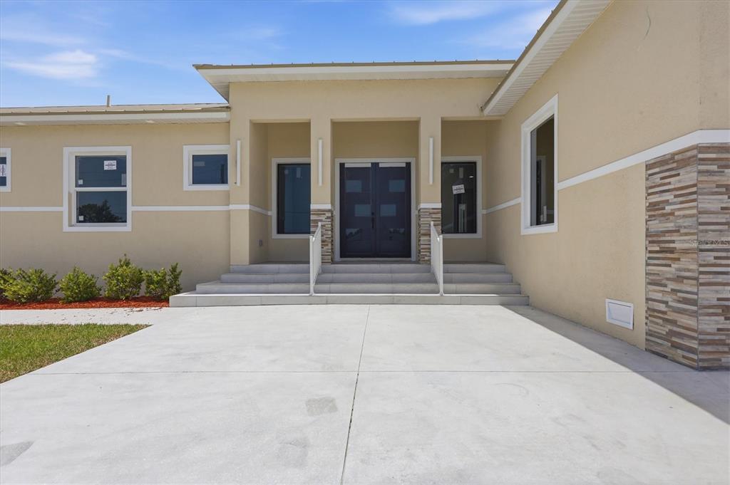 The exterior of a beige house features a concrete driveway, stone accents, and double doors — 14491 INGRAHAM BOULEVARD, PORT CHARLOTTE, FL