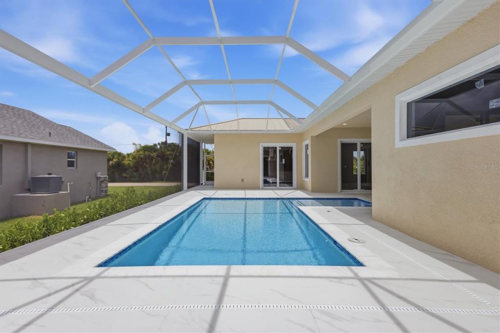 A rectangular swimming pool sits on a white tiled patio enclosed by a screened lanai — 14491 INGRAHAM BOULEVARD, PORT CHARLOTTE, FL