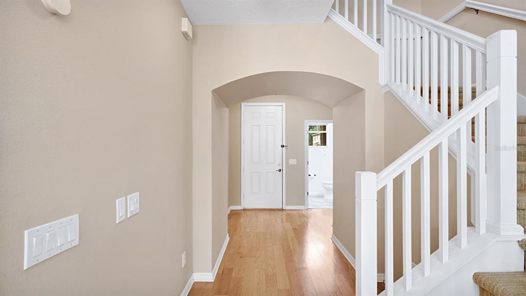 An entryway with hardwood floors, a white staircase, and a doorway leading to a bathroom — 412 PENNY ROYAL PLACE, OVIEDO, FL