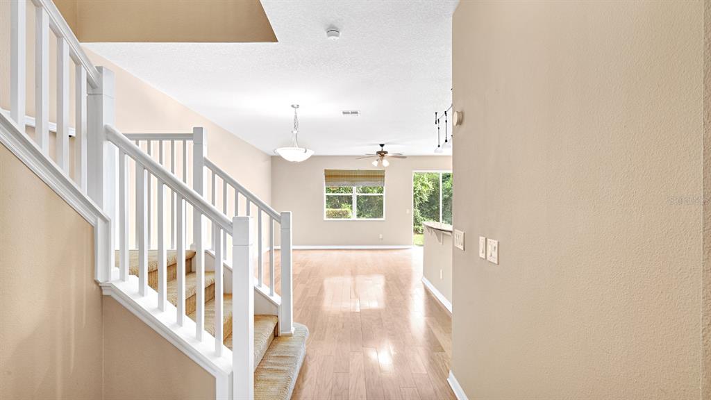 A staircase with white railings leads to an open-concept living area with light wood flooring — 412 PENNY ROYAL PLACE, OVIEDO, FL