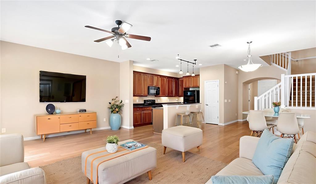 An open-concept living room and kitchen feature hardwood floors, wooden cabinetry, and a staircase — 412 PENNY ROYAL PLACE, OVIEDO, FL