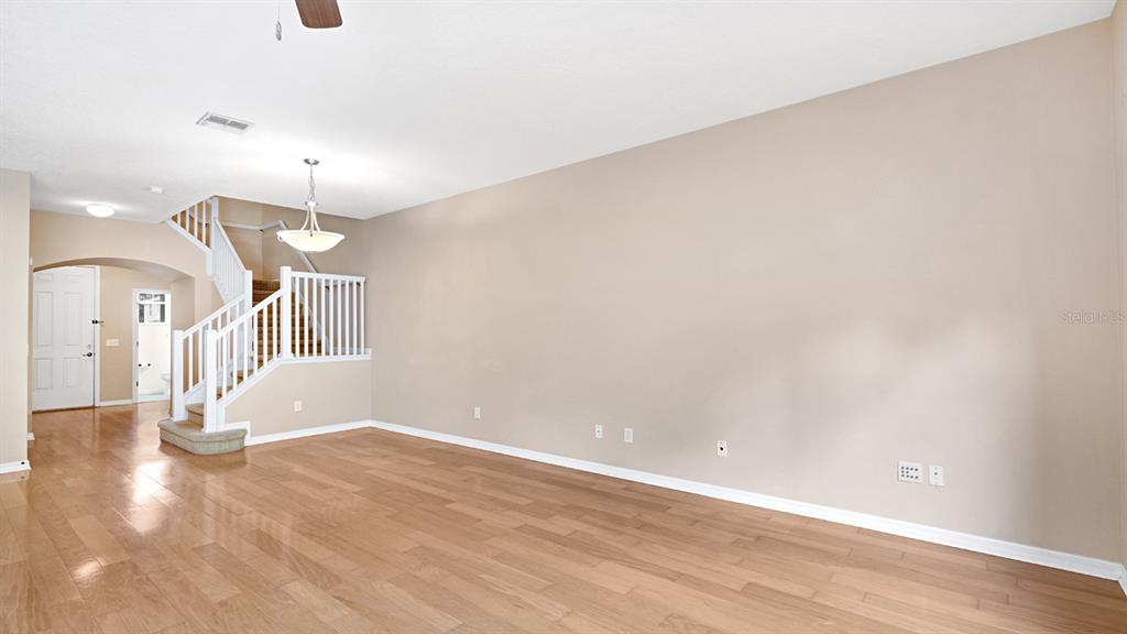 An empty living room features light wood flooring, beige walls, and a white staircase — 412 PENNY ROYAL PLACE, OVIEDO, FL