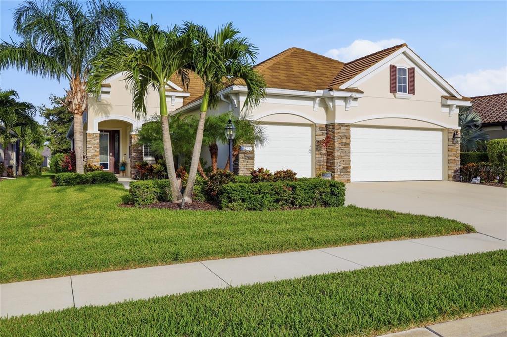A single-story house with a tan stucco exterior, stone accents, and a three-car garage — 4209 MIDNIGHT BLUE RUN, BRADENTON, FL