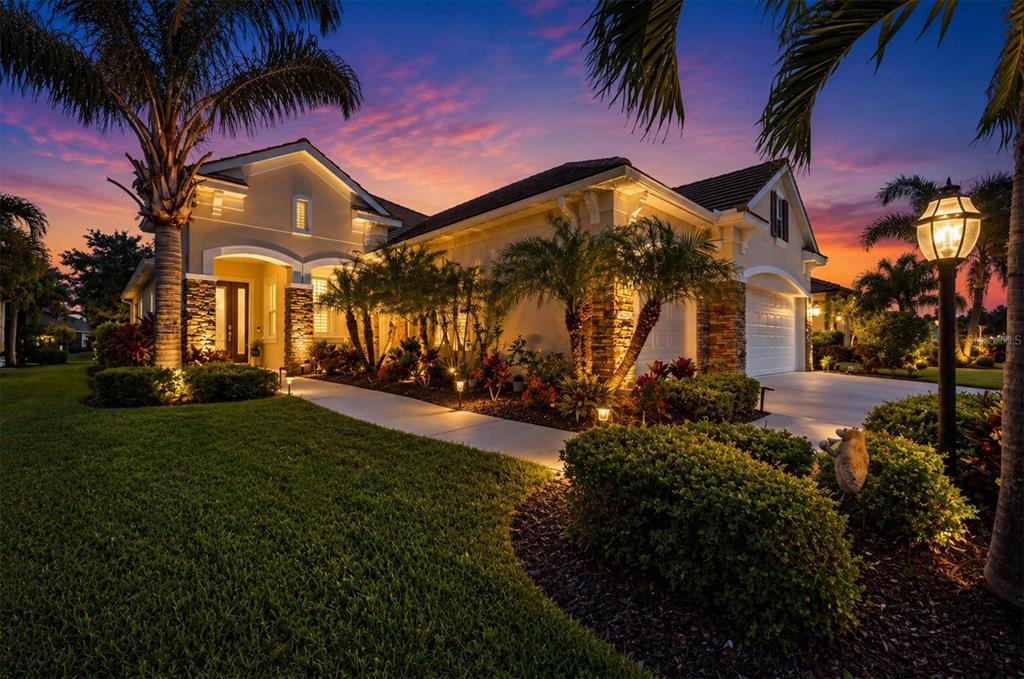 A single-story house with a palm tree, manicured lawn, and stone accents at twilight — 4209 MIDNIGHT BLUE RUN, BRADENTON, FL