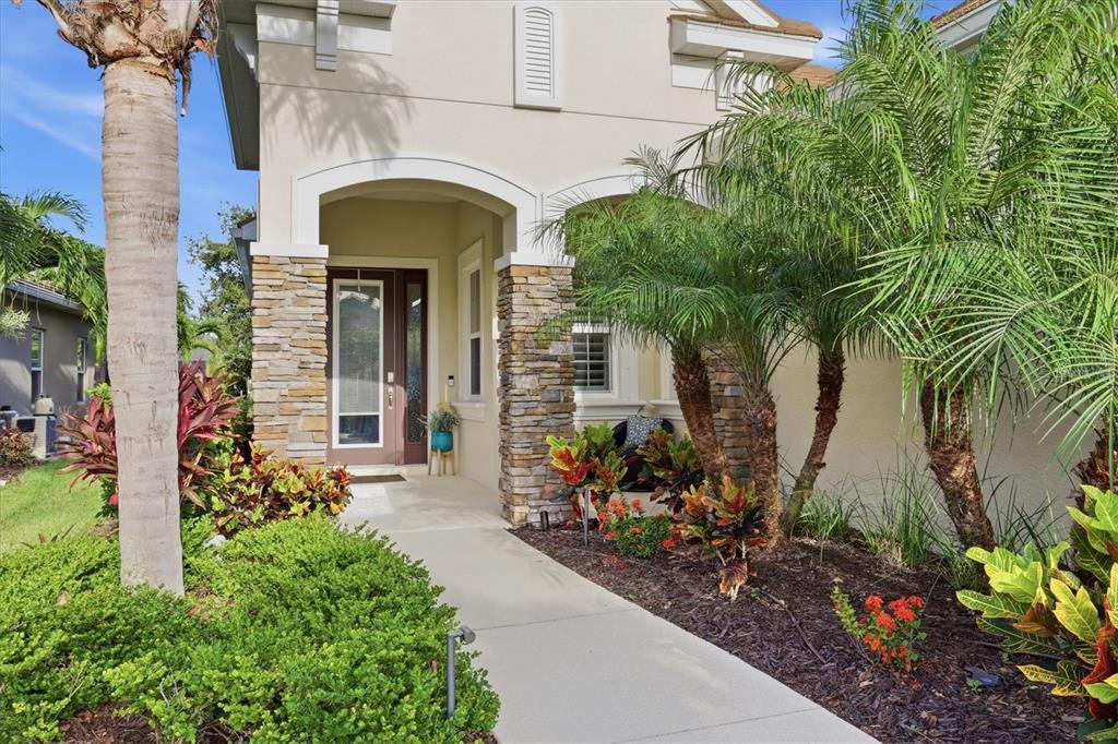A stone-accented entryway leads to a front door with a glass panel and palm landscaping — 4209 MIDNIGHT BLUE RUN, BRADENTON, FL
