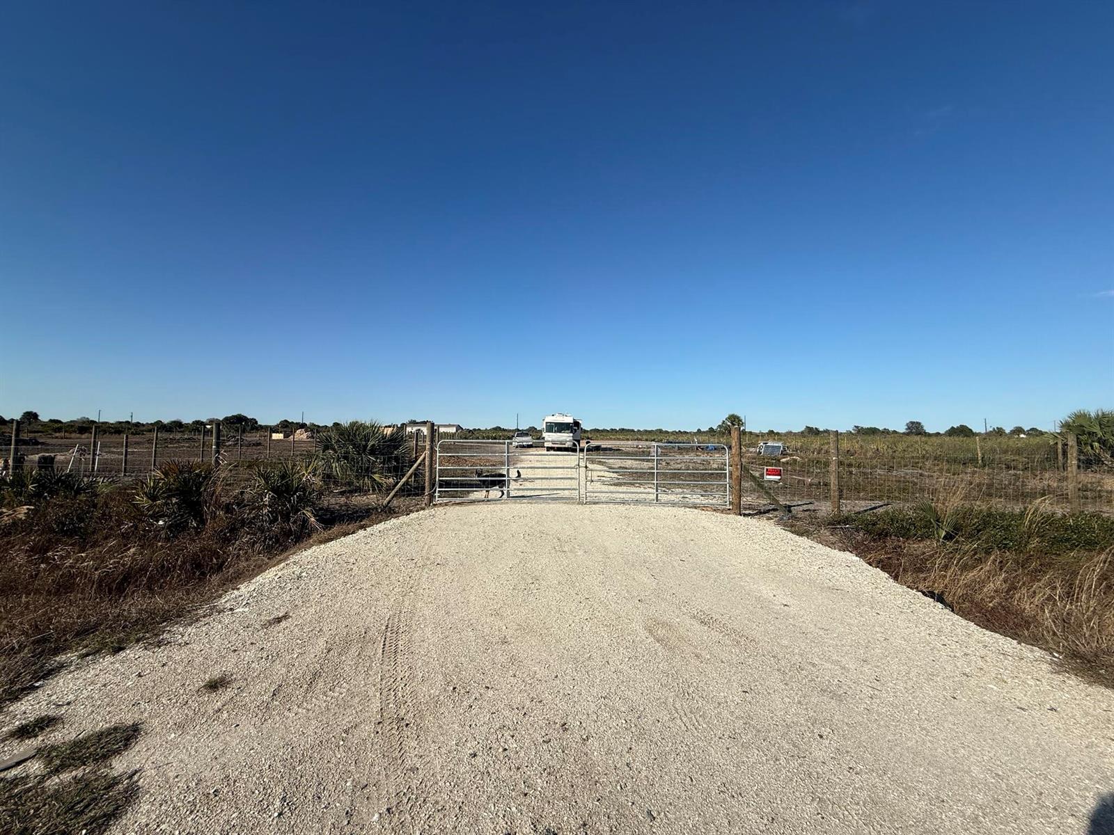 A gravel driveway leads to a metal gate and a parked RV on open land — 21377 NW 276th Street, Okeechobee FL 34972, OKEECHOBEE, FL