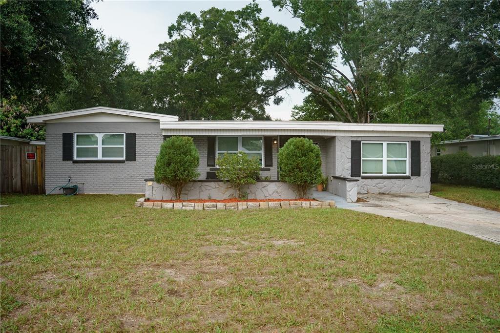 A single-story gray brick house features a front porch, a low stone wall, and landscaping — 10906 N LANTANA AVENUE, TAMPA, FL
