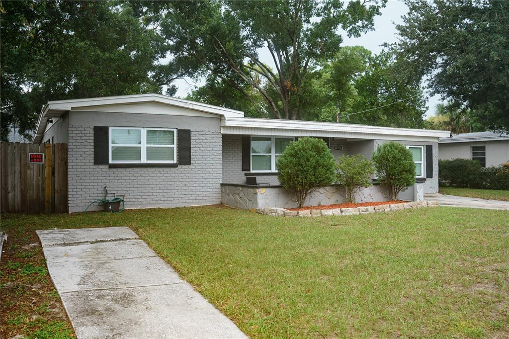 A single-story gray brick house features a front porch, landscaping, and a concrete driveway — 10906 N LANTANA AVENUE, TAMPA, FL