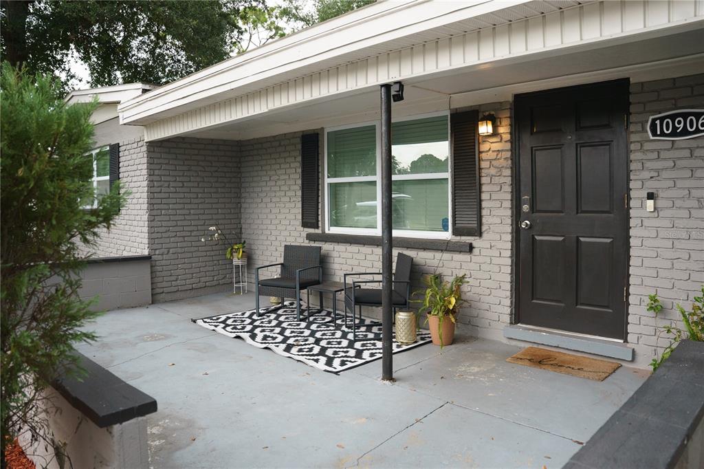 A gray brick house exterior features a covered concrete porch with two chairs and rug — 10906 N LANTANA AVENUE, TAMPA, FL