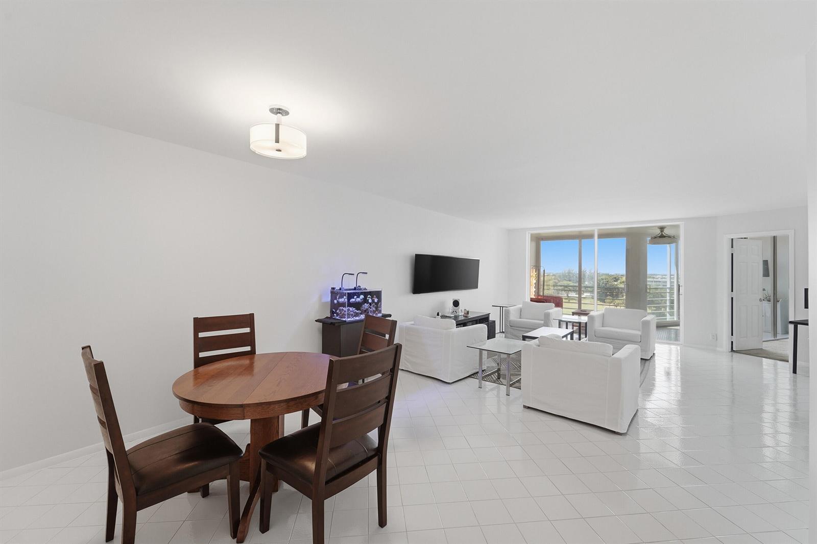 A bright, open-concept living and dining area features white tile flooring and a balcony view — 2681 S Course Drive # 808, Pompano Beach FL 33069, POMPANO BEACH, FL