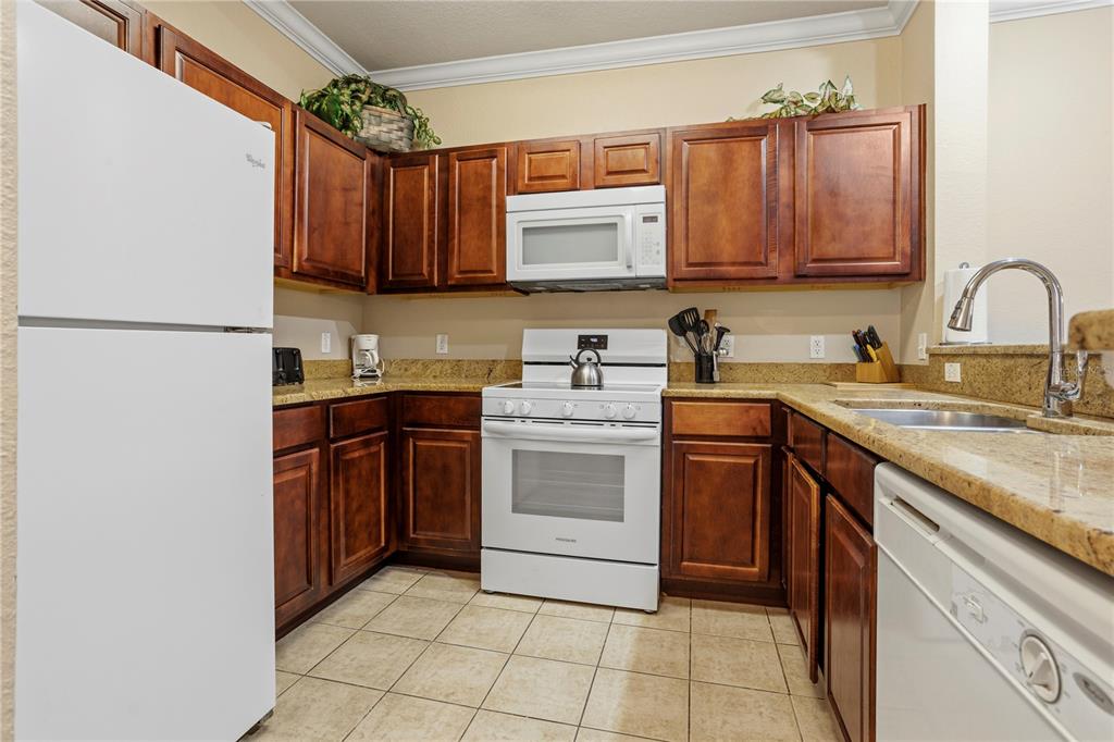 A kitchen features dark wood cabinets, white appliances, granite countertops, and light tile flooring — 1370 TUSCAN TERRACE UNIT 2308, DAVENPORT, FL