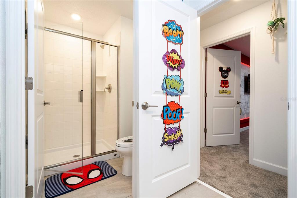 A bathroom with a glass-enclosed shower, a toilet, and comic-themed decor on the door — 4383 SCENE LANE, KISSIMMEE, FL