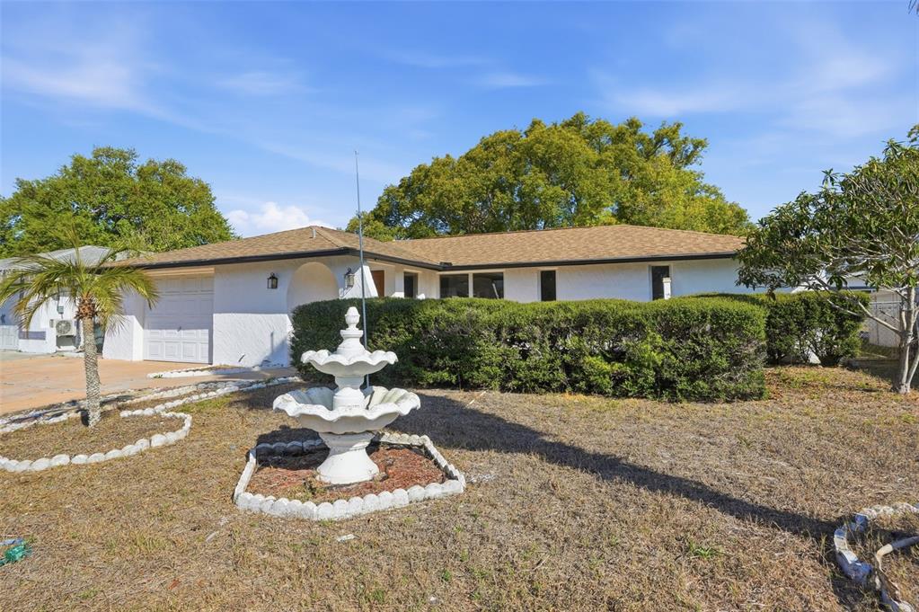 A white single-story house features a tiered fountain in the front yard and a hedge — 7427 FIRESIDE DRIVE, PORT RICHEY, FL