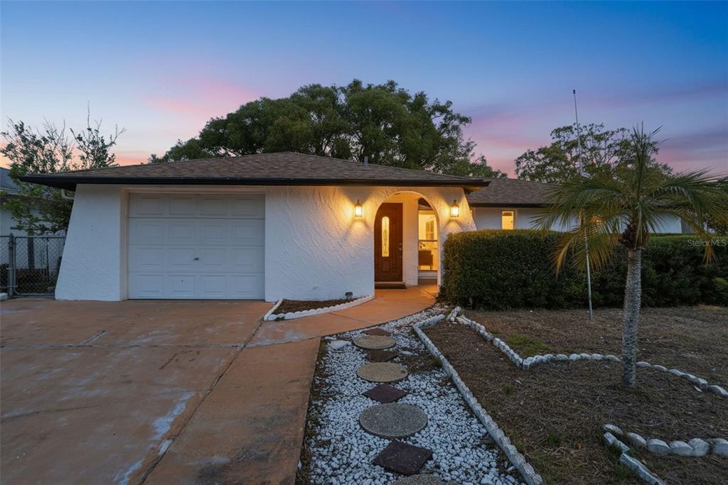 A white stucco house with a single-car garage and a stone-lined walkway at dusk — 7427 FIRESIDE DRIVE, PORT RICHEY, FL