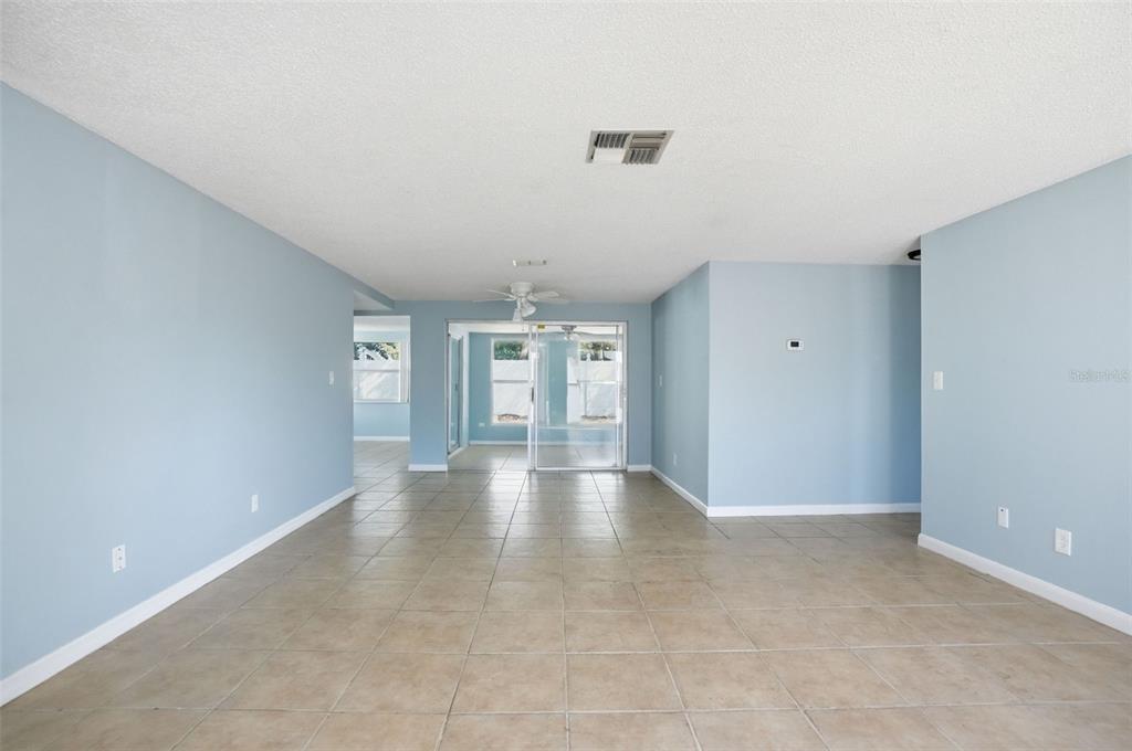 An open-concept living area features light blue walls, tan floor tiles, and a sliding door — 7427 FIRESIDE DRIVE, PORT RICHEY, FL