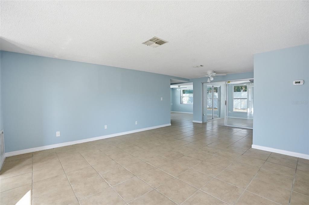 An empty room with light blue walls, beige tile flooring, and sliding glass doors — 7427 FIRESIDE DRIVE, PORT RICHEY, FL