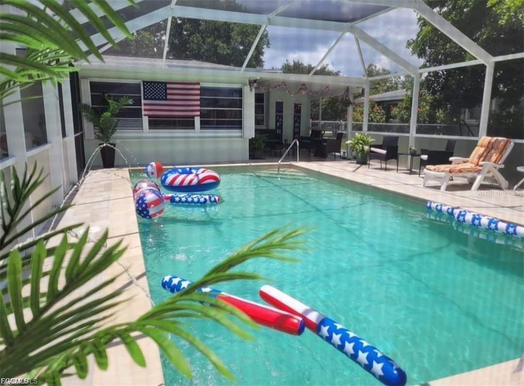 A screened-in swimming pool features patriotic-themed pool floats and an American flag on the house — 2705 SE 17TH AVENUE, CAPE CORAL, FL
