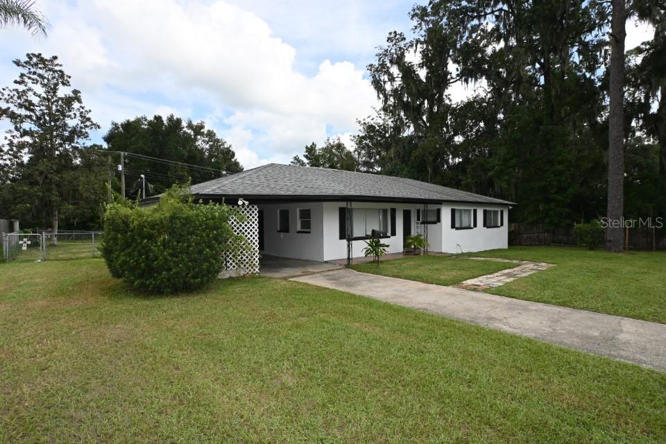 A single-story white house with a carport, a concrete driveway, and a large front lawn — 37017 MERIDIAN AVENUE, DADE CITY, FL