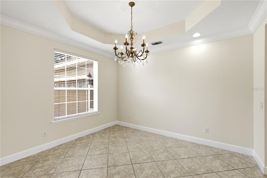 A dining room with a tray ceiling, crystal chandelier, tile flooring, and a large window — 3205 KING GEORGE DRIVE, ORLANDO, FL