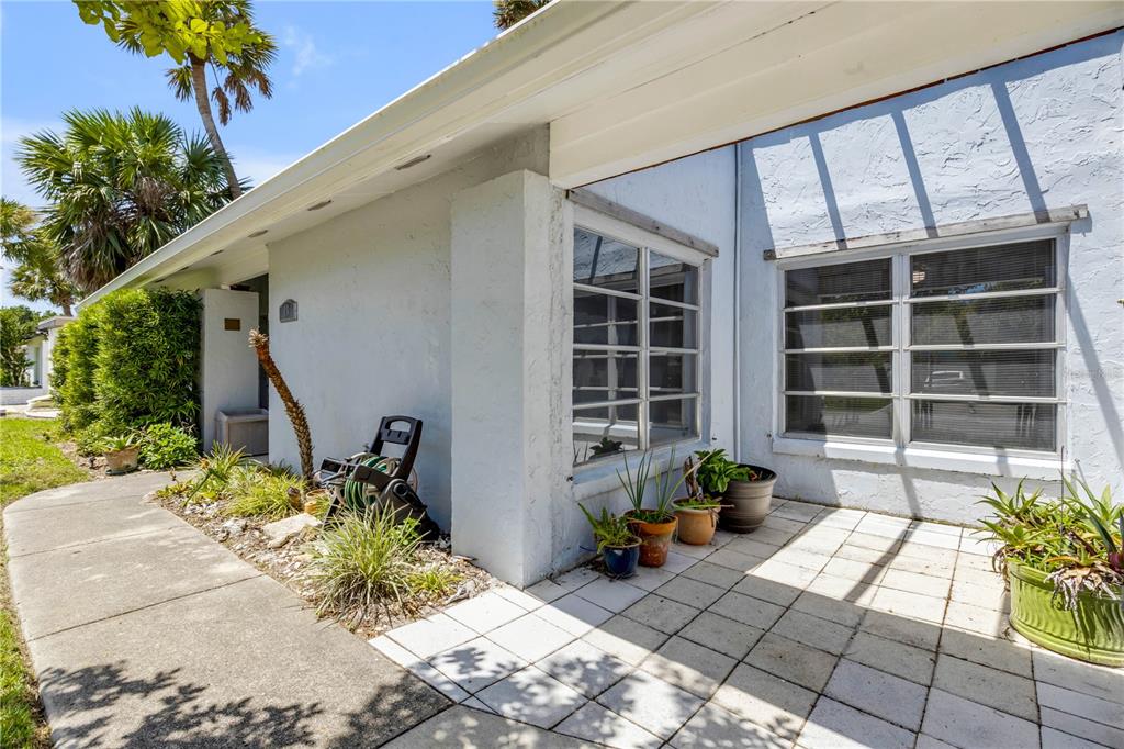 A light blue exterior wall features a tiled patio, two windows, and several potted plants — 19 CROMPTON PLACE, PALM COAST, FL
