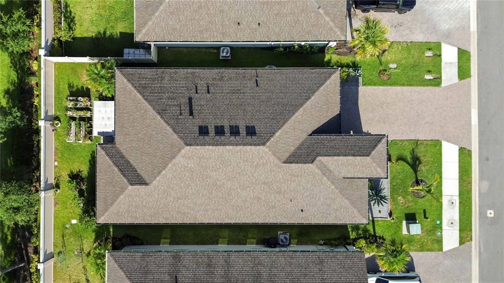 An aerial view shows the shingled roof of a house with solar panels and landscaping — 14814 SORA WAY, BRADENTON, FL