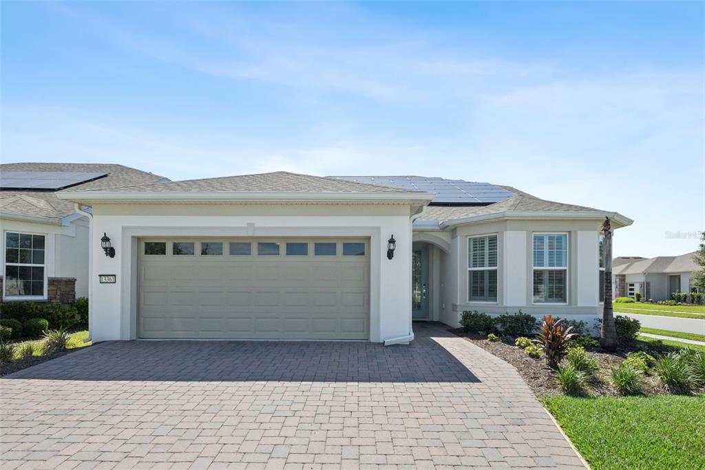 A single-story house with a paved driveway, a two-car garage, and solar panels on the roof — 13361 SUNNY RETREAT LANE, WINTER GARDEN, FL
