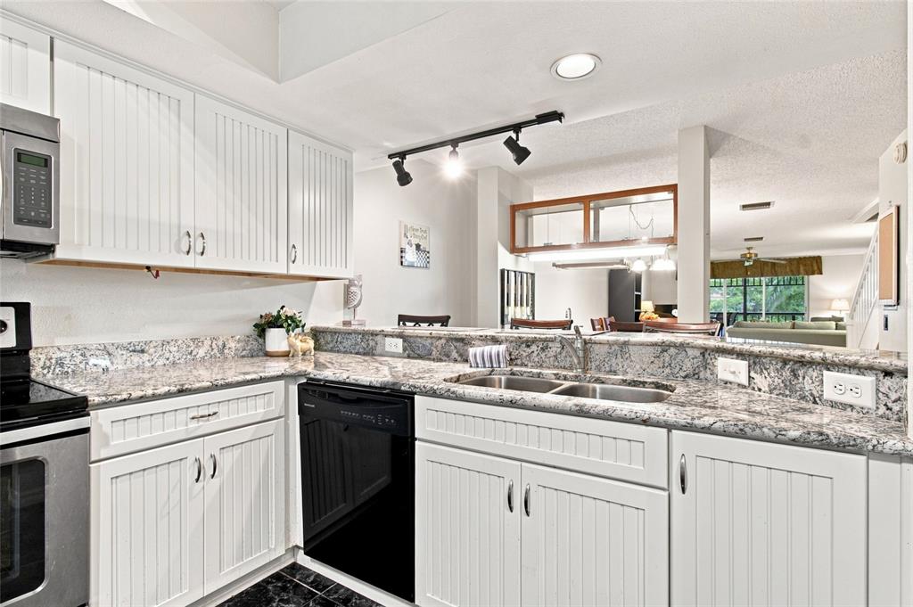 A kitchen features white beadboard cabinetry, granite countertops, a black dishwasher, and stainless steel appliances — 2599 DOLLY BAY DRIVE UNIT 306, PALM HARBOR, FL