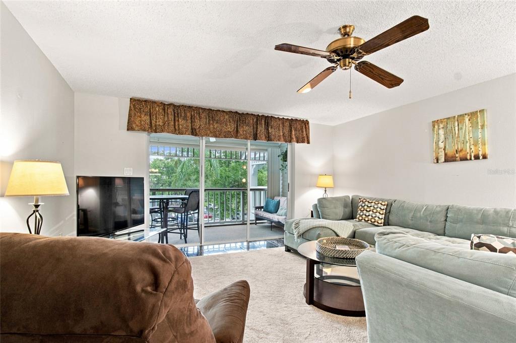A living room features a sectional sofa, a ceiling fan, and a balcony with outdoor seating — 2599 DOLLY BAY DRIVE UNIT 306, PALM HARBOR, FL