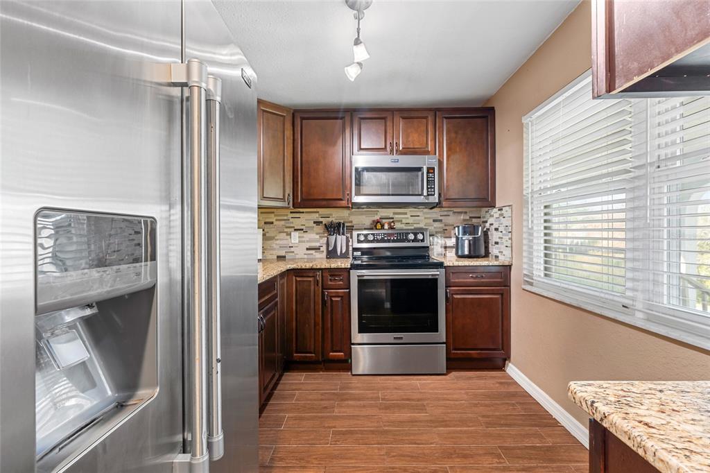 A kitchen features dark wood cabinets, stainless steel appliances, granite countertops, and wood-look tile flooring — 1303 S HERCULES AVENUE UNIT 25, CLEARWATER, FL