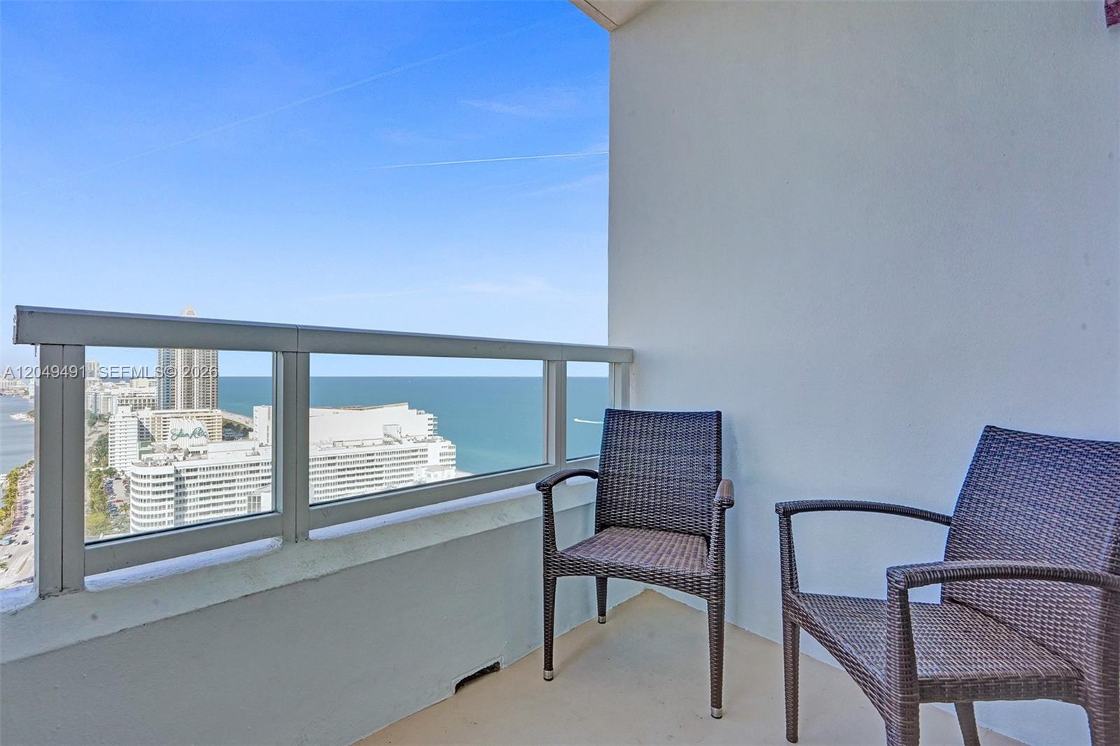 A balcony with two wicker chairs overlooks a coastal city and the ocean — 4401 Collins Ave # 2915, Miami Beach FL 33140, MIAMI BEACH, FL