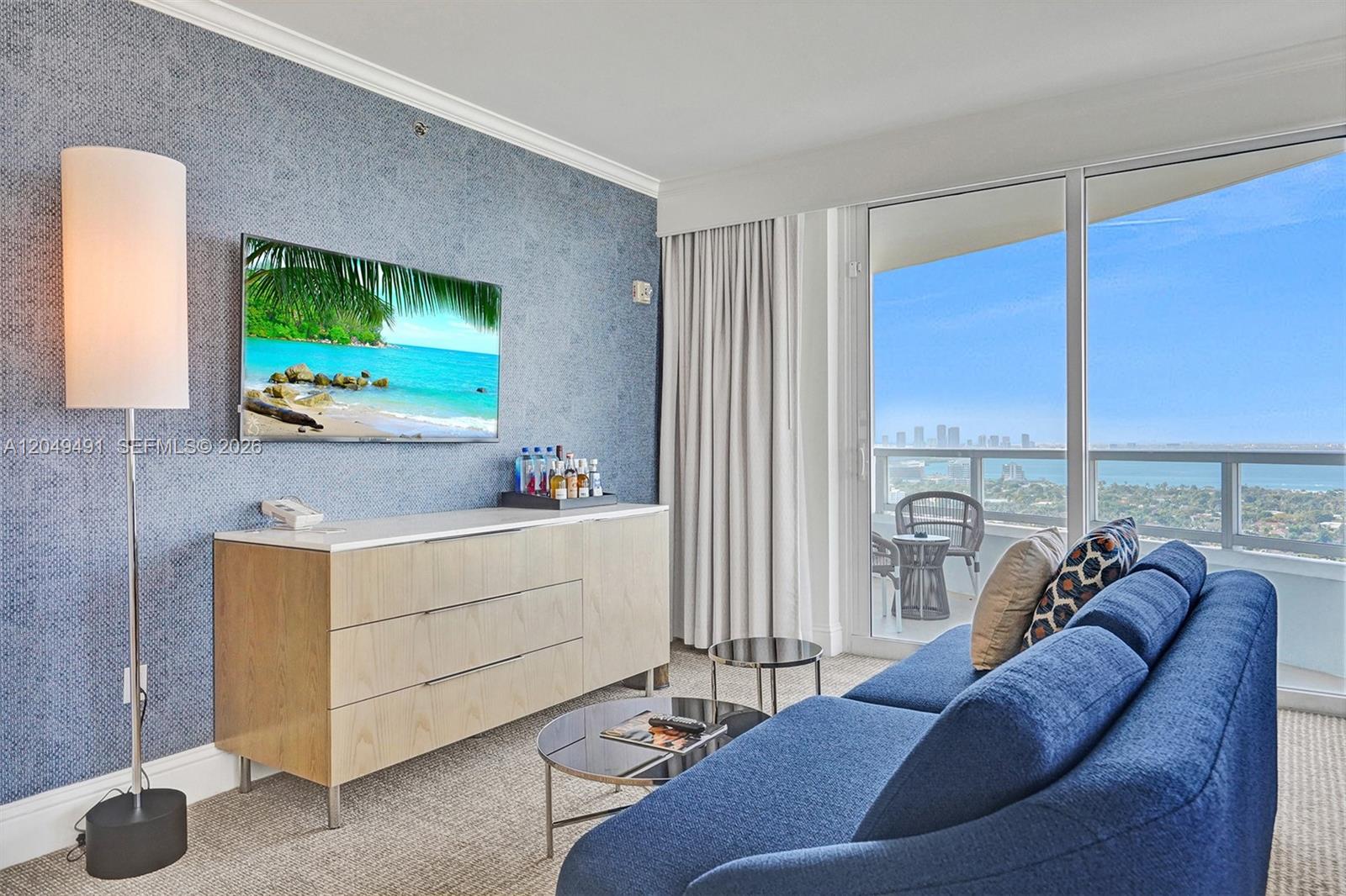 A living room features a blue textured wall, a sofa, a dresser, and a balcony view — 4401 Collins Ave # 2915, Miami Beach FL 33140, MIAMI BEACH, FL