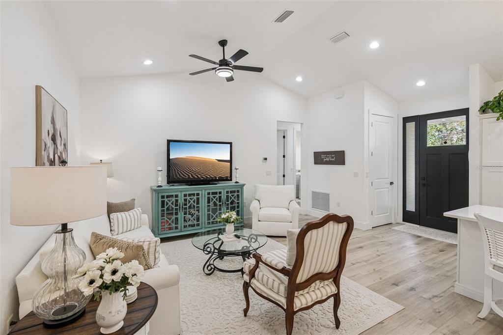 A living room features white walls, light wood floors, a teal media console, and neutral furniture — 11722 LAKE MINNEOLA SHORES, MINNEOLA, FL