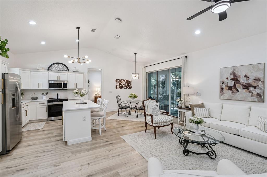 An open-concept kitchen, dining area, and living room featuring white cabinetry and light wood flooring — 11722 LAKE MINNEOLA SHORES, MINNEOLA, FL