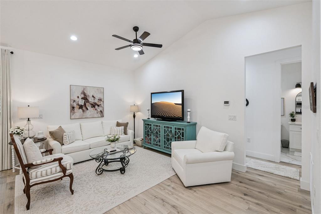 A living room features a white sofa, armchair, patterned accent chair, and a teal media console — 11722 LAKE MINNEOLA SHORES, MINNEOLA, FL