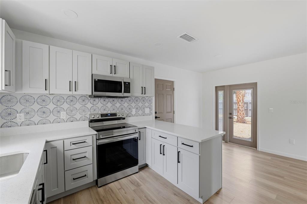 A kitchen with white cabinets, stainless steel appliances, patterned backsplash, and light wood flooring — 3030 5TH STREET N, ST PETERSBURG, FL