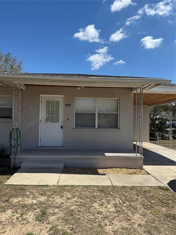 The exterior of a single-story house features a concrete porch, white door, and metal awning — 1247 LAKEVIEW DRIVE, CLERMONT, FL