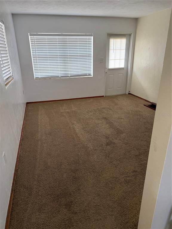 An empty room with brown carpet, white walls, a large window, and a glass-paneled door — 1247 LAKEVIEW DRIVE, CLERMONT, FL