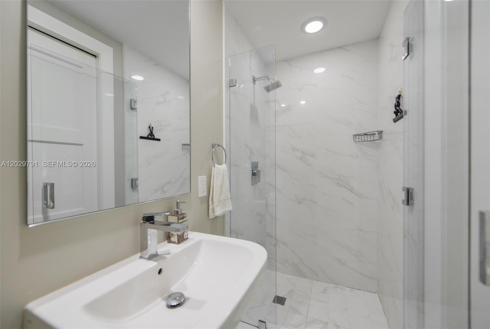 A modern bathroom features a white pedestal sink, a glass-enclosed shower, and marble-style tile — 801 S Miami Ave # 3706, Miami FL 33130, MIAMI, FL