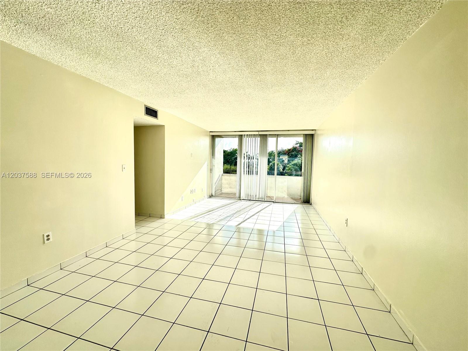 An empty room features white tile flooring, a popcorn ceiling, and a sliding glass door — 802 NW 87th Ave # 315, Miami FL 33172, MIAMI, FL