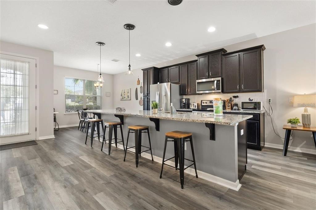 A kitchen features dark wood cabinets, granite countertops, a gray island with stools, and flooring — 1594 CAREY PALM CIRCLE, KISSIMMEE, FL