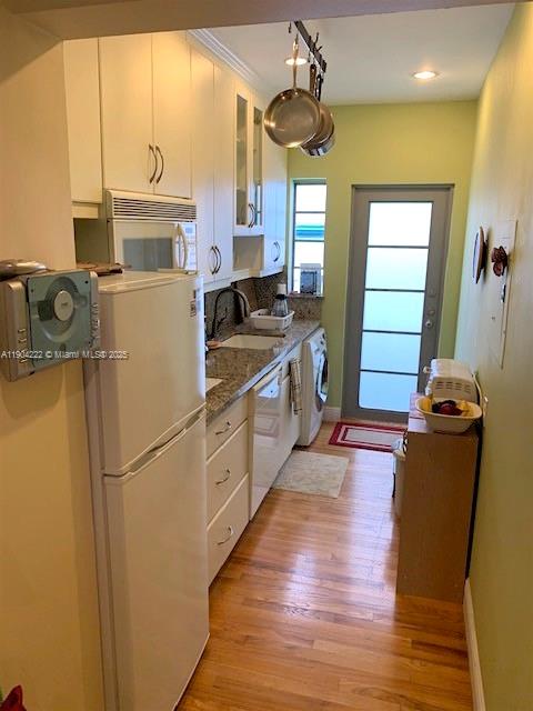 A narrow kitchen features white cabinets, a refrigerator, wood flooring, and a glass-paneled door — 744 Lenox Ave # 3, Miami Beach FL 33139, MIAMI BEACH, FL