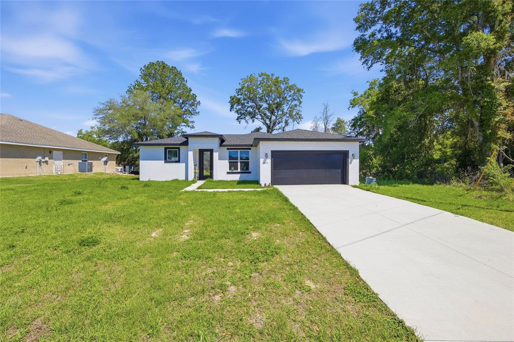 A single-story white house with a dark garage door and a concrete driveway — 4411 SW 132ND PLACE, OCALA, FL