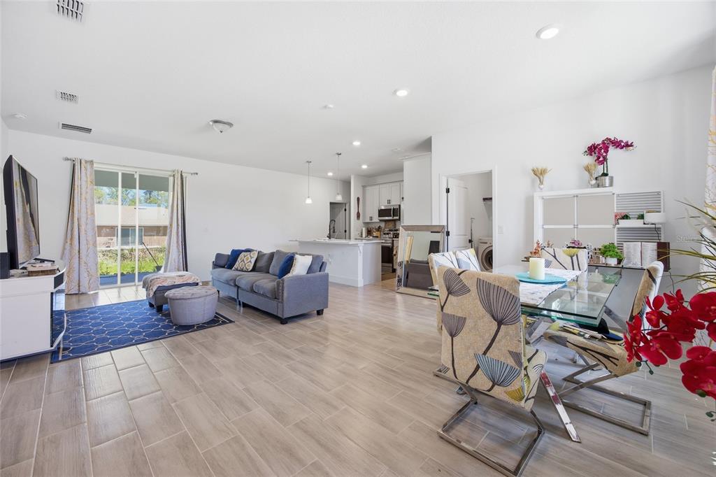 An open-concept living and dining area features light wood-look tile floors and a modern kitchen — 4411 SW 132ND PLACE, OCALA, FL