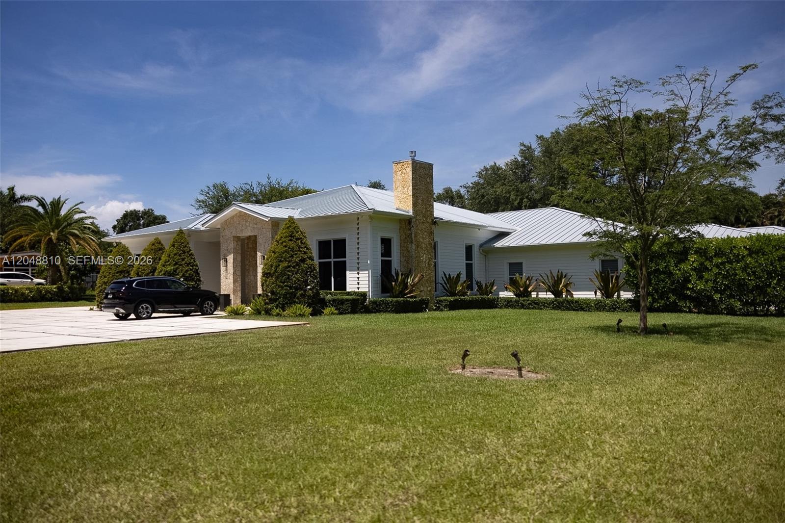 A white single-story house with a metal roof and stone chimney sits on a lawn — 9805 sw 90th ave, Kendall FL 33176, KENDALL, FL