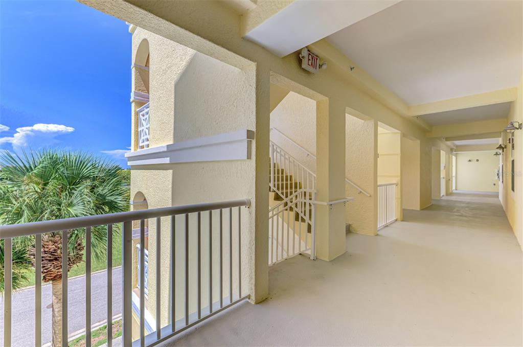 An outdoor apartment building walkway features a staircase, white railings, and a view of palm trees — 8571 AMBERJACK CIRCLE UNIT 204, ENGLEWOOD, FL