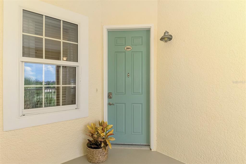 A teal front door with the number 204 sits beside a window on a stucco porch — 8571 AMBERJACK CIRCLE UNIT 204, ENGLEWOOD, FL