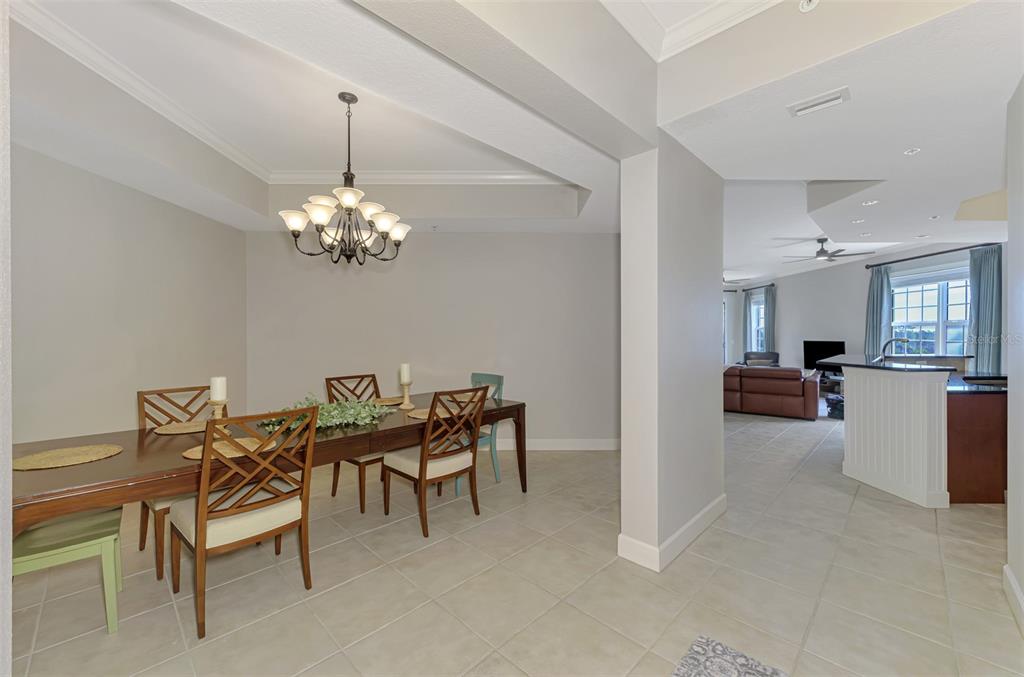 A dining room with a chandelier and wooden chairs opens into a living area — 8571 AMBERJACK CIRCLE UNIT 204, ENGLEWOOD, FL