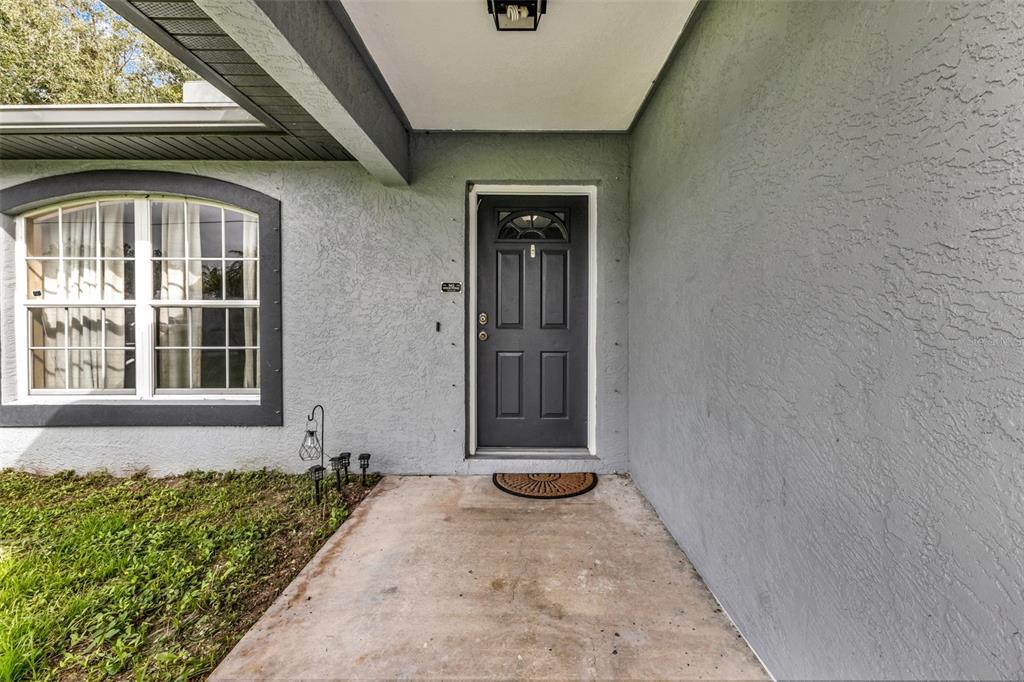 A gray front door with a small window sits under a covered porch next to a window — 3237 CLEARFIELD STREET, NORTH PORT, FL