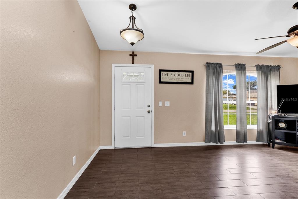 A living room features dark wood-look tile flooring, a white front door, and gray curtains — 3237 CLEARFIELD STREET, NORTH PORT, FL